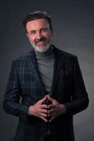 Portrait of a stylish elegant senior businessman with a beard and casual business clothes in photo studio isolated on dark background gesturing with hands