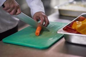 chef en la cocina del hotel cortar verduras con cuchillo foto