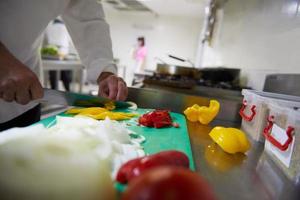 chef en la cocina del hotel cortar verduras con cuchillo foto