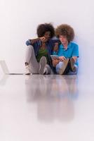 pareja multiétnica sentada en el suelo con una laptop y una tableta foto