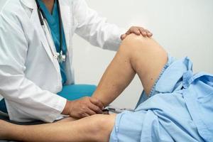 Asian doctor physiotherapist examining, massaging and treatment knee and leg of senior patient in orthopedist medical clinic nurse hospital. photo