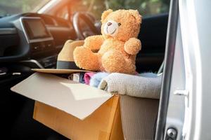 Volunteer woman provide clothing donation box with used clothes and doll at home to support help for refugee, homeless or poor people in the world. photo