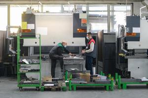 two workers wearing a protective mask due to a coronavirus pandemic, working in a modern factory and preparing a program and materials for a cnc machine photo