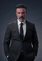 Portrait of a stylish elegant senior businessman with a beard and casual business clothes in photo studio isolated on dark background gesturing with hands