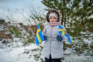 Scandinavian baby girl with Sweden flag in winter swedish landscape. photo