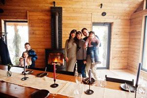 Family with four kids in modern wooden house against table and fireplace, spending time together in warm and love. photo