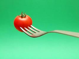 fresh tomato on fork with green background photo