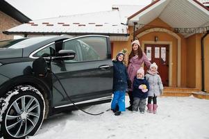 Young woman with kids hold eco bags and charging electric car in the yard of her house . photo