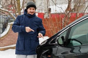 Young man charging his electric car in winter. Eco transport concept. photo