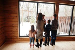 madre y cuatro hijos en una casa de madera moderna contra una ventana grande. foto