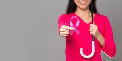 octubre mes de concientización sobre el cáncer de mama, mujer adulta con vestido rosa mano sosteniendo cinta rosa y paraguas para apoyar la protección. espacio de copia del concepto del día internacional de la mujer, la madre y el día mundial del cáncer foto