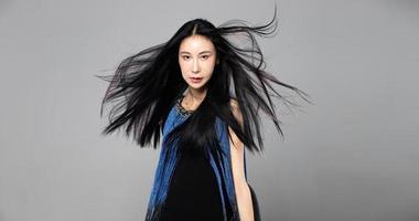 Asian Transgender Woman with long black straight hair, wind blow throw in the Air. Female spin turn around and wear blue fashion sensual sexy dress, gray background isolated copy space photo