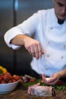 chef poniendo sal en una jugosa rebanada de bistec crudo foto