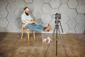 creación de contenidos para redes sociales. hombre barbudo filmando un video de sí mismo usando una cámara en un trípode. tecnología moderna y concepto de trabajo independiente de blogs. foto