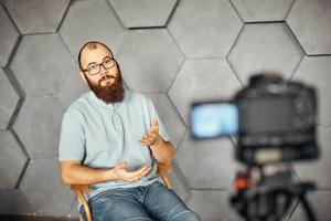 creación de contenidos para redes sociales. hombre barbudo filmando un video de sí mismo usando una cámara en un trípode. tecnología moderna y concepto de trabajo independiente de blogs. foto