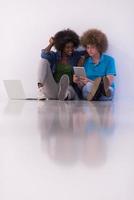 multiethnic couple sitting on the floor with a laptop and tablet photo