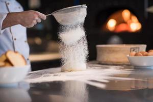 chef sprinkling flour over fresh pizza dough photo