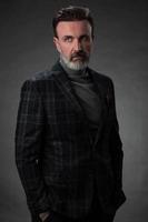 Portrait of a stylish elegant senior businessman with a beard and casual business clothes in photo studio isolated on dark background gesturing with hands