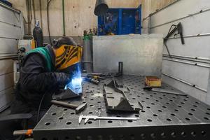 soldador profesional realiza trabajos con piezas metálicas en fábrica, chispas y electricidad. pancarta de trabajadores de la industria. foto