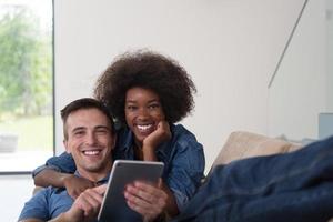 pareja multiétnica relajándose en casa con tabletas foto