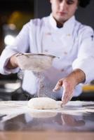 chef sprinkling flour over fresh pizza dough photo