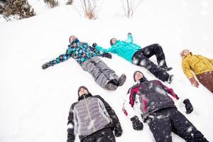 grupo de jóvenes tirados en la nieve y haciendo ángel de nieve foto