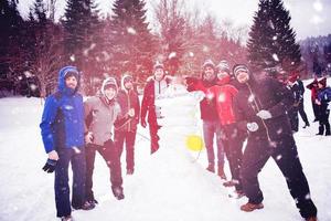 group portait of young people posing with snowman photo