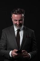 Portrait of adult businessman wearing trendy suit and sitting in modern studio on stylish chair against the black background photo