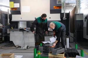 two workers wearing a protective mask due to a coronavirus pandemic, working in a modern factory and preparing a program and material for a cnc machine photo