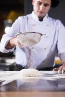 chef sprinkling flour over fresh pizza dough photo