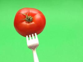 fresh tomato on fork with green background photo