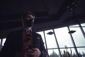 hombre de negocios con mascarilla médica de coronavirus mientras usa un teléfono inteligente foto