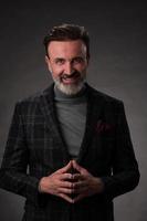 Portrait of a stylish elegant senior businessman with a beard and casual business clothes in photo studio isolated on dark background gesturing with hands