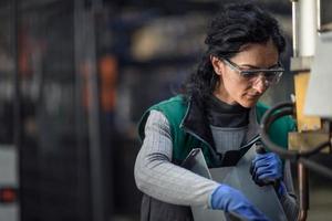 mujer trabajadora con gafas de seguridad controla la máquina de torno para perforar componentes. fábrica de fabricación industrial de torno de metal foto