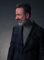 Portrait of a stylish elegant senior businessman with a beard and casual business clothes in photo studio isolated on dark background gesturing with hands