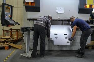 dos hombres que trabajan en una industria moderna preparan material para procesar en una máquina cnc, usan una máscara protectora en la cara debido a una pandemia de virus coronario foto