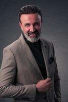 Portrait of a stylish elegant senior businessman with a beard and casual business clothes in photo studio isolated on dark background gesturing with hands