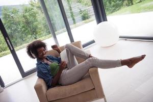 mujer afroamericana en casa en silla con tableta y auriculares foto