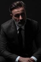 Portrait of a stylish elegant senior businessman with a beard and casual business clothes in photo studio isolated on dark background gesturing with hands