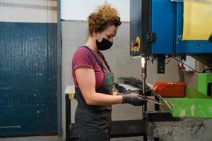 mujer con mascarilla debido a la pandemia del coronavirus mientras trabaja en la industria metalúrgica moderna y usa taladro foto