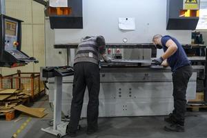 two workers wearing a protective mask due to a coronavirus pandemic, working in a modern factory and preparing a program and materials for a cnc machine photo