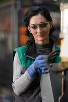 mujer trabajadora con gafas de seguridad controla la máquina de torno para perforar componentes. fábrica de fabricación industrial de torno de metal foto