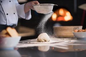 chef sprinkling flour over fresh pizza dough photo