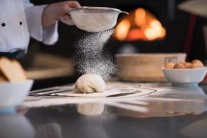 chef sprinkling flour over fresh pizza dough photo