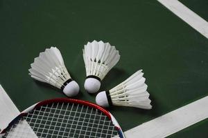 Cream white badminton shuttlecock and racket on red floor in indoor badminton court, copy space, soft and selective focus on shuttlecocks. photo