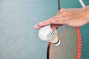 Badminton player holds racket and white cream shuttlecock in front of the net before serving it to another side of the court. photo