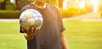 un viejo fútbol sosteniendo en la mano del jugador, enfoque suave y selectivo en el fútbol, fondo editado por la luz del sol. foto