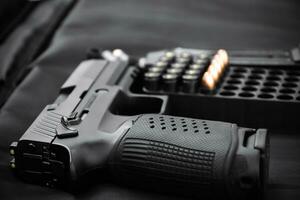 Automatic black 9mm pistol and bullets on black leather background, selective and soft focus. photo