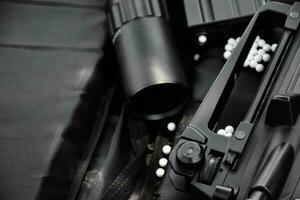 Airsoft gun or BB gun equipments, bullets, gun body, and binocular on dark leather floor background, soft and selective focus. shooting sports and recreational activity concept. photo