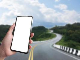 White blank touch screen smartphone holding in hand with blurr modern  buildings background. Close up view of right hand with mobile device. Mock up, copyspace, template and technology concept. photo